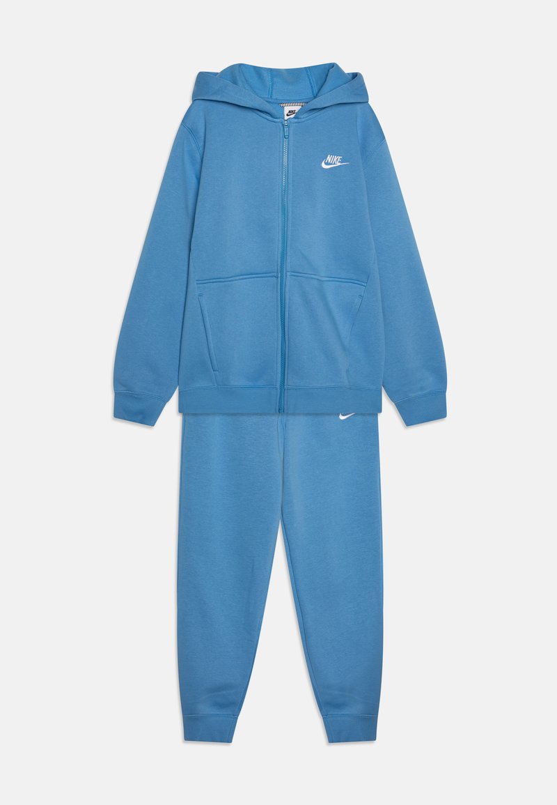 Nike zilā kapuce ar rāvējslēdzēju un kabatām, ar baltu logo uz krūtīm. Kopā ar atbilstošām zilām sporta biksēm ar elastīgām galvām.
