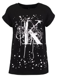 Camiseta de manga corta negra con diseño de salpicaduras blancas y grandes letras "CK" blancas, texto "Calvin Klein Jeans" en la parte frontal.