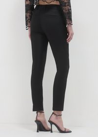 Pantaloni neri aderenti con una texture liscia, dotati di due tasche posteriori e vita a metà altezza. Indossati con tacchi alti neri con cinturini.