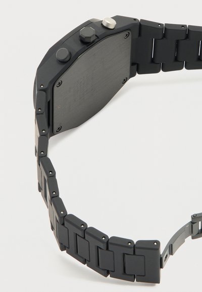 Μαύρο μεταλλικό ρολόι χειρός που δείχνει την πίσω θήκη με βίδες και ένα μεταλλικό λουρί με συνδέσμους, καμπυλωμένο σε ημικύκλιο σε λευκό φόντο.