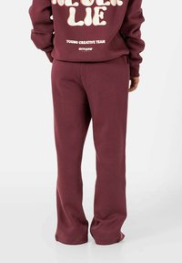 Bordeaux sweatshirt en bijpassende sweatpants. De sweatshirt heeft grote witte tekst op de achterkant. De broek heeft een relaxte pasvorm en een zachte textuur.
