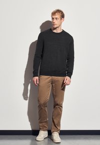 Dunkelgrauer Strickpullover, hellbraune Chinos und beige Sneaker. Die Texturen sind glatt mit einem figurbetonten Design und Rundhalsausschnitt.