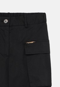Svarte cargoshorts med elastisk linning, knappeåpning, en sidelomme og en gulllogoakcent på lomma. Jevn stofftekstur.