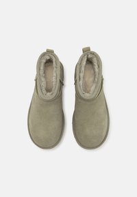 Bottines en daim vert avec une doublure douce en fausse fourrure, bout arrondi et détails de couture latérale. Aucune quincaillerie ou accent visible.