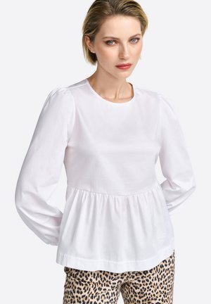 Blouse blanche à manches longues avec un col rond, des épaules froncées et une taille peplum, associée à un pantalon à imprimé léopard.