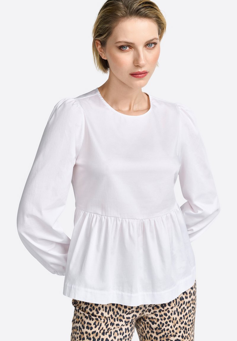 Blusa bianca a maniche lunghe con scollatura rotonda, spalle arricciate e vita a peplo, abbinata a pantaloni a stampa leopardata.