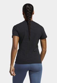 Czarny t-shirt z krótkim rękawem widziany z tyłu, wykonany z bawełny, o prostym kroju i gładkiej fakturze. Połączony z niebieskimi legginsami sportowymi.