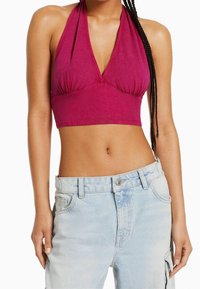 Fuchsia beskuren halterneck-topp med djup V-ringning och plisserad detalj, ihopparad med ljusblå högmidjade jeans med knäppning.