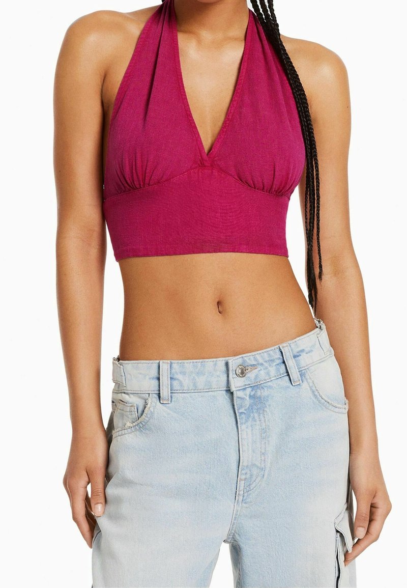 Fuchsia beskuren halterneck-topp med djup V-ringning och plisserad detalj, ihopparad med ljusblå högmidjade jeans med knäppning.