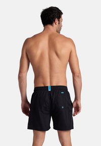 Bañadores negros con una cintura elástica y un pequeño acento azul en la parte trasera. La tela parece ligera y suave al tacto.