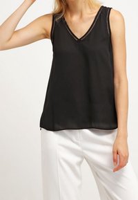 Top nero senza maniche con scollatura a V e cuciture decorative lungo il colletto, realizzato in un tessuto liscio e leggero.