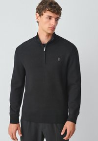 Schwarzer Zip-Pullover mit gerippten Bündchen, Rundhalsausschnitt und Logoakzent auf der Brust. Hergestellt aus strukturiertem Strickstoff.