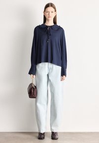 Μπλε ναυτικό τοπ με μακριά μανίκια, γιακά με βολάν και κορδέλα, ανοιχτό μπλε τζιν ψηλόμεσο, και μπορντό τσάντα χειρός. Μαύρα μποτάκια αστραγάλου ολοκληρώνουν την εμφάνιση.