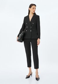 Blazer negro a rayas finas, ajustado, con botones de doble botonadura, combinado con pantalones negros de corte slim y tacones negros de punta. Se incluye un bolso elegante.