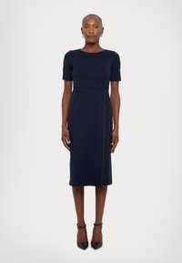 Tengerészkék, térdihosszú ruha rövid ujjakkal. Testhezálló felsőrész, övvarrással deréknál és egyenes sziluettel. Simaság, minimál dizájn.