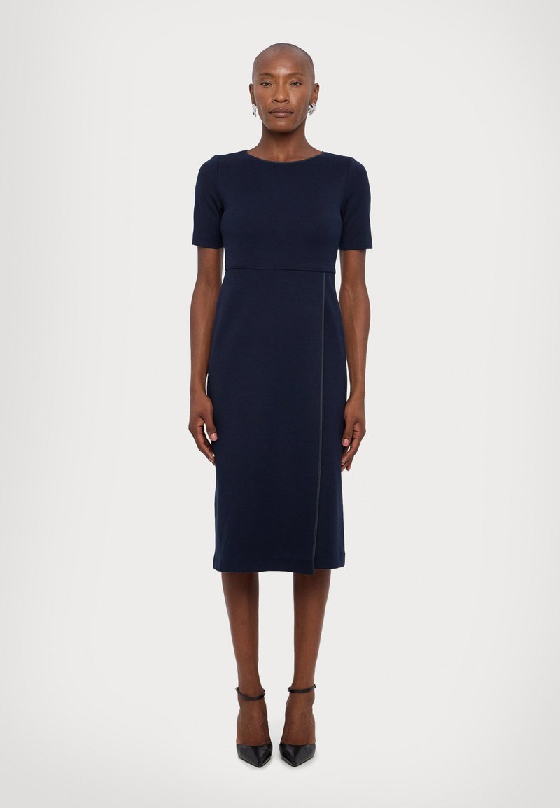 Robe bleu marine, longueur genou, avec des manches courtes. Corsage ajusté, détail de couture à la taille et silhouette droite. Texture lisse, design minimal.