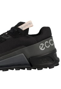 Schwarze Sneaker mit strukturiertem Obermaterial, Gore-Tex-Logoetikett und grauen Akzenten. Verfügt über eine dicke Sohle mit markantem Traktionsmuster und Branding.