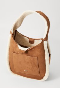 Sac à épaule en daim marron avec bordures en fourrure blanche, poche frontale, fermeture à pression et logo DKNY sur la poche avant.