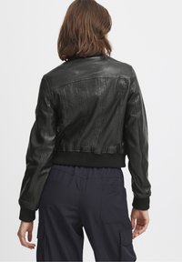 Černá kožená zkrácená bunda s žebrovanými manžetami a lemem, zdobená švovými detaily na zádech. Hladká textura, minimalistický design.