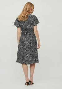 Rochie cu puncte negre și albe, cu mâneci scurte și fluturate, lungime până la genunchi și talie ajustată. Materialul pare ușor, cu un design casual.
