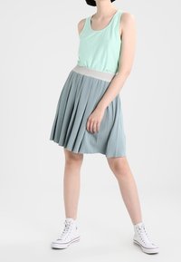 En mintgrön linne tillsammans med en ljusblå plisserad kjol med en texturerad midja. Vita högskurna sneakers fulländar outfiten.