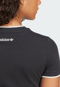 Černé bavlněné tričko s bílými akcenty na límci a logem na zadní straně. Přiléhavý střih s krátkými rukávy, hladká textura.