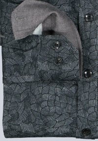 Nahaufnahme eines gefalteten dunklen Hemdes mit geometrischem Muster und kontrastierenden hellgrauen Stoff im Kragen und an den Manschetten.