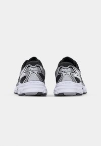 Black and silver athletic shoes with a mesh upper, padded collar, and white rubber soles. Features curved accents and textured detailing.