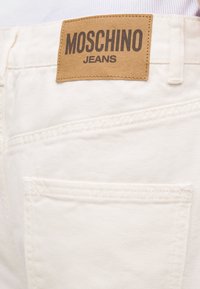 Λευκό τζιν παντελόνι με πίσω τσέπη και καφετί ετικέτα της μάρκας Moschino Jeans ραμμένη πάνω από την τσέπη.