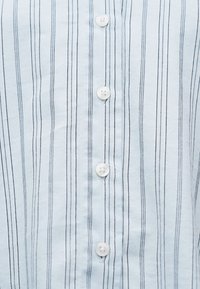 Υφασμα ανοικτού γαλάζιου με λεπτές κάθετες ναυτικές και λευκές ρίγες, με μια κεντρική σειρά από λευκά κουμπιά.