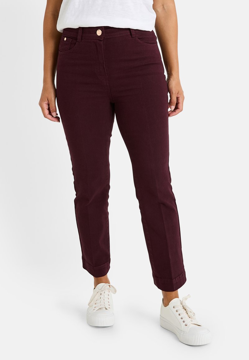 Jeans de stretch burdeos con un corte ajustado, que presentan bolsillos frontales y un dobladillo enrollado. Combinados con zapatillas blancas para un contraste.