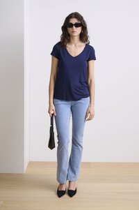 Tengerészkék V-nyakú póló világoskék harangszárú farmernadrággal, fekete hegyes orrú magassarkú cipővel és egy kis fekete táskával párosítva. A modellen fekete napszemüveg van.