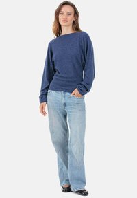 Marineblauer Pullover mit weitem Ausschnitt und langen Ärmeln, kombiniert mit hellblauen, lockeren Jeans und schwarzen Schuhen. Glatte Textur, lässige Passform.