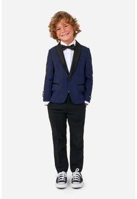 Chaqueta de esmoquin azul marino con solapas de satén negro, camisa blanca, pajarita negra, pantalones negros y zapatillas negras con cordones blancos.