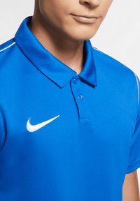 Modrá polokošile Nike s klasickým límcem, dvěma knoflíky a bílým logem na levé hrudi. Hladká, strukturovaná tkanina s kontrastními pruhy.