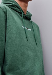 Grön hoodie i mjukt tyg, med snörning i huvan och broderad "TOMMY JEANS"-logotyp med färgdetaljer.