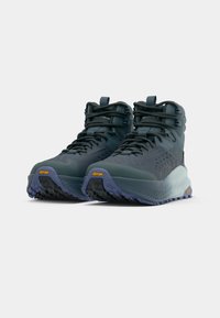 Sapatos de basquete de cano alto em verde-escuro com superfícies texturizadas, atacadores pretos e uma sola Vibram com detalhes em roxo e amarelo.
