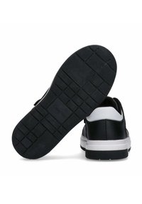 Sneaker in bianco e nero con suola in gomma texturizzata, caratterizzate da una forma curva e una tomaia in pelle liscia con un dettaglio del logo sul tallone.