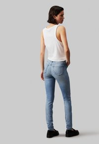 Világoskék, enyhén kopott skinny farmernadrág, hátul zsebekkel. Fehér ujjatlan felsővel és fekete cipővel párosítva.