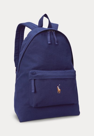 Tumši zils mugursoma ar priekšējo rāvējslēdzēja kabatu un nelielu izšūtu logotipu ar polo spēlētāju uz zirga, diviem augšējiem rāvējslēdzēju aizdares galiņiem un polsterētiem plecu siksnām.