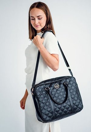 Schwarze gesteppte Handtasche mit doppelten Griffen, goldfarbenem Logo-Akzent und verstellbarem Schultergurt. Glatte Textur und strukturiertes Design.