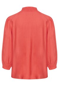 Blusa corallo con collo alto, dettagli smockati al colletto e maniche a sbuffo. Tessuto morbido e vestibilità rilassata e ampia.