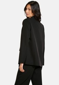 Črn blazer iz gladkega materiala, z sproščenim krojem in odprtim sprednjim delom. Opremljen je z dolgimi rokavi in subtilnim razporkom na hrbtu.