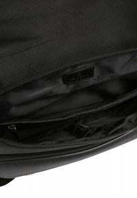 Zwarte nylon tas interieur met zichtbare compartimenten. Geweven stof, gladde ritsluiting en een leren label. Ruimtelijk en minimalistisch ontwerp.