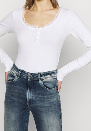 Witte body met lange mouwen en kantafwerking bij de halslijn, met een knoopsluiting, gecombineerd met blauwe denim jeans. Glad materiaal, aansluitend model.