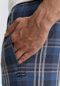 Blaue karierte Shorts mit beigen Akzenten, seitlicher Tasche, weichem Stoff und sichtbarem Markenschild auf der linken Seite.