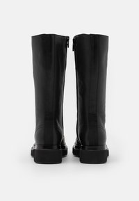 Bottes en cuir noir montantes avec une finition lisse, dotées de deux fermetures éclair à l'arrière et d'un solide talon bloc. La semelle est texturée pour une meilleure adhérence.