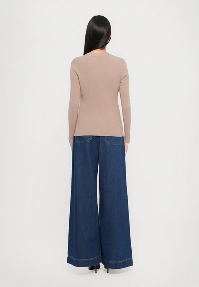 Top a maniche lunghe rigato di color marrone chiaro abbinato a pantaloni in denim blu a gamba larga, dotati di vita alta e tasche posteriori in vista.