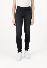 Juoda slim fit džinsai, pagaminti iš džinsinio audinio, su aukštu liemeniu, dviem priekinėmis kišenėmis ir dviejų mygtukų užsegimu. Su baltais sportbačiais.