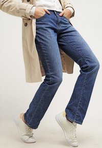 Mäntäkkä siniset farkut napilla, denim-materiaalia, keskikorkea vyötärö ja hienovarainen haalistuminen. Yhdistetty vaaleisiin lenkkareihin.